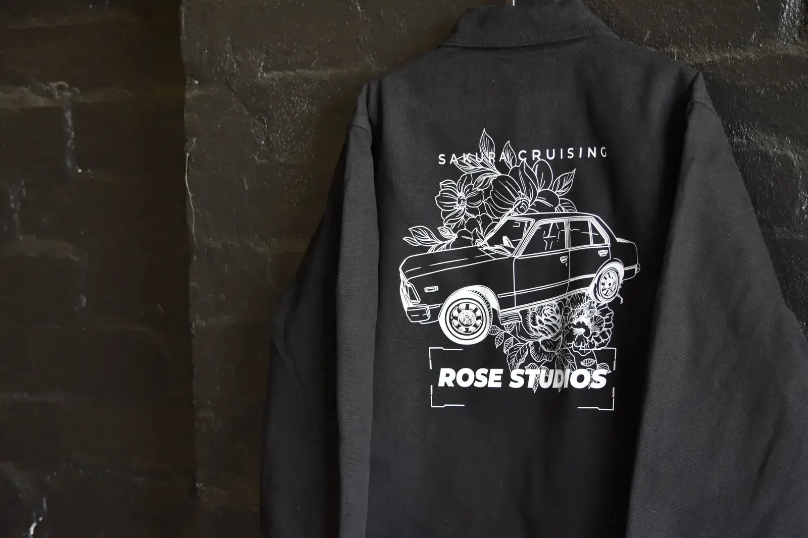 Rose Studios black zip hoodie with embroidered logo on dark brick wall